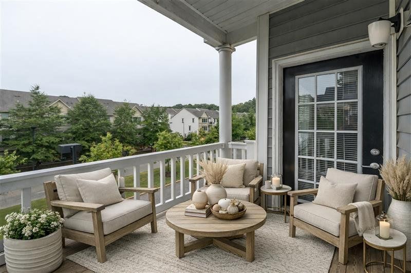 Cozy porch with beige cushioned chairs, round table, potted plants, and candles overlooking neighborhood houses.
