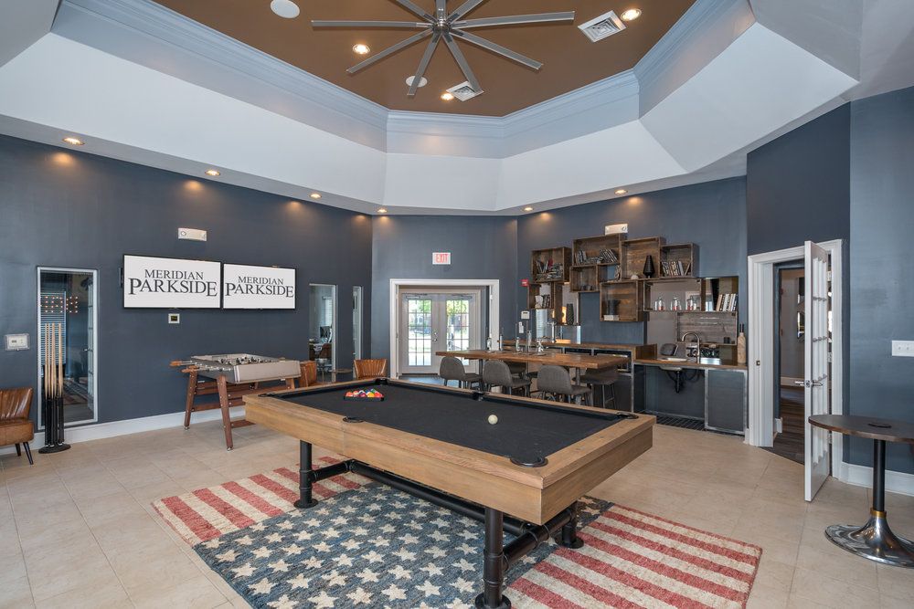 Modern game room with a pool table, foosball, lounge seating, and shelves, featuring a large ceiling fan.