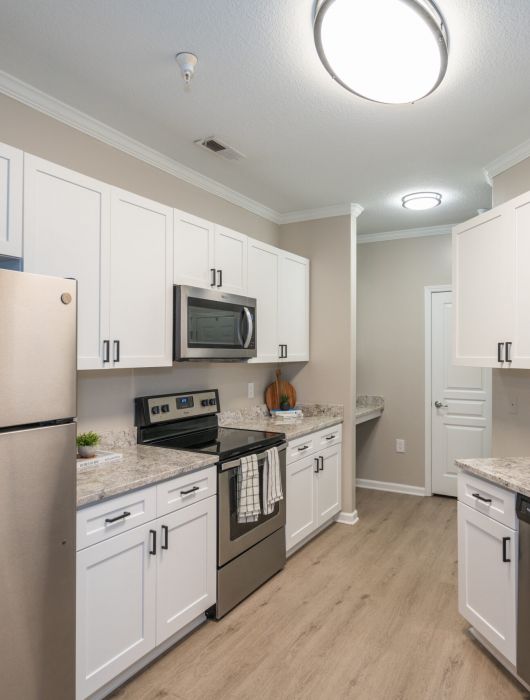 Modern kitchen with white cabinets, stainless steel appliances, marble countertops, and light wood flooring.