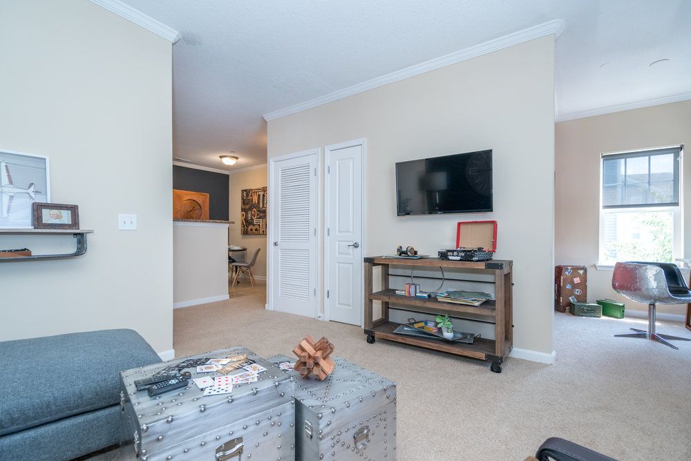 A living room with beige walls, a TV on the wall, and metal storage trunks used as a coffee table.