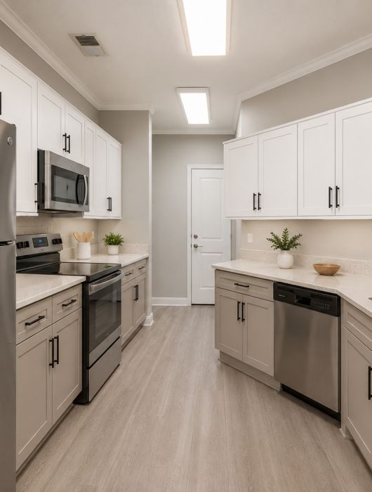 Modern kitchen with white cabinets, stainless steel appliances, and light wood flooring.