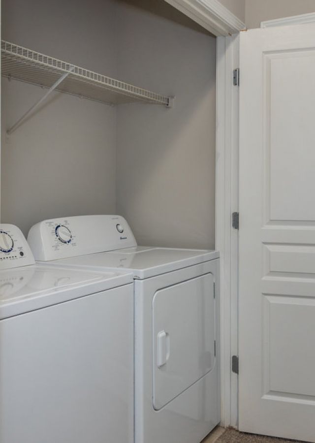 A laundry area with a white washing machine and dryer, open double doors, and an empty wire shelf above.