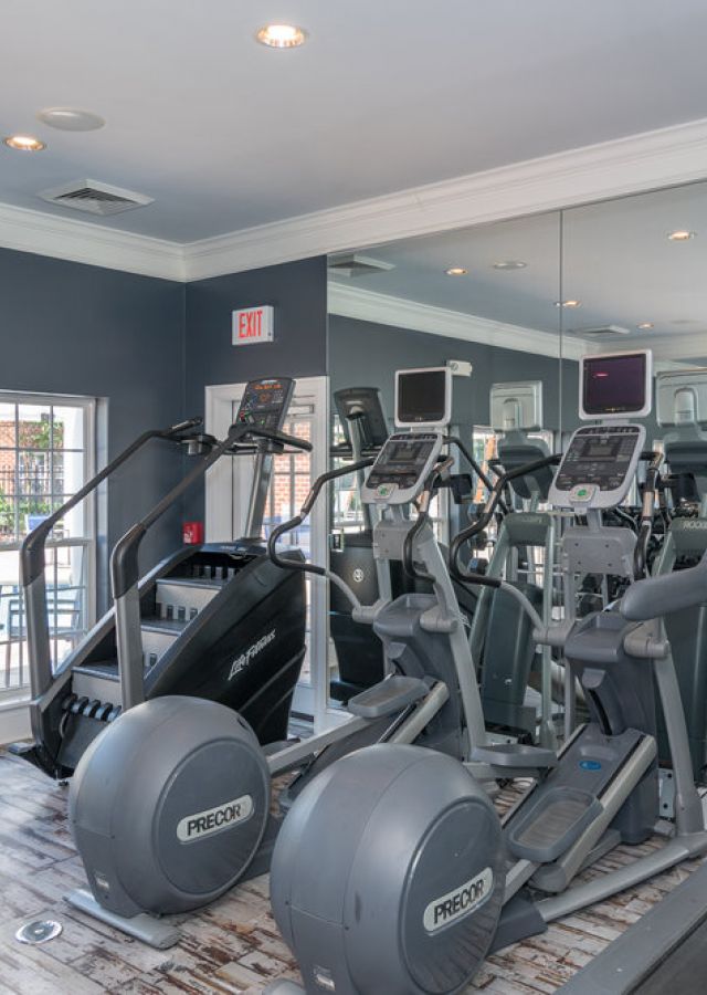 Modern gym with treadmills, ellipticals, weights, and mirrors, with windows overlooking a pool area.